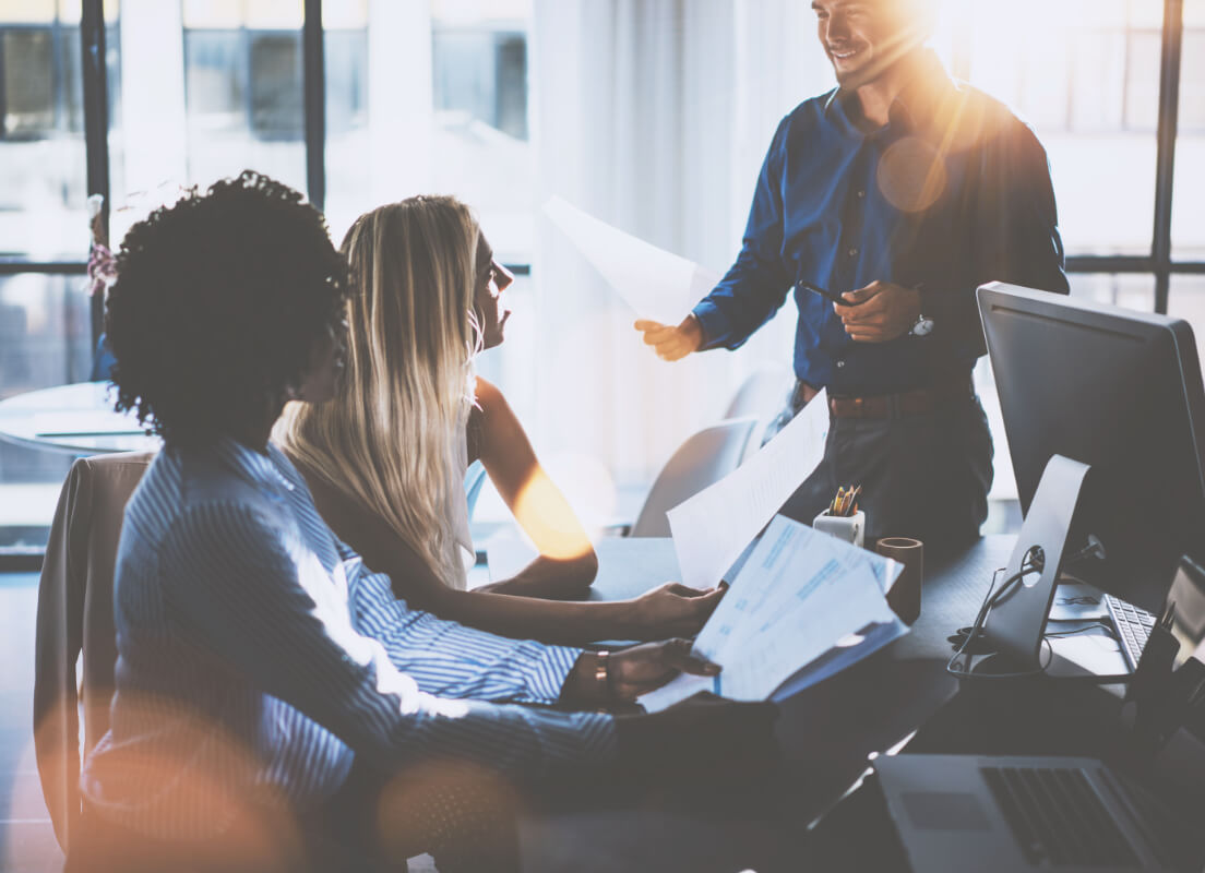 three people holding bits of paper talking in an office