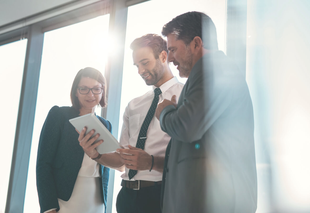 three cheerful people looing at a tablet in an office